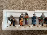 Seven Dept 56 collectible porcelain figurines in original white styrofoam packaging showing front views.