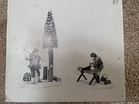 Photo of two porcelain lumberjack figurines; one chopping with an axe, one sawing wood, resting on white snow-like bases