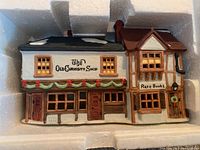 Front and top view of Dept 56 ceramic building named The Old Curiosity Shop, showing snow on roof and painted signage.