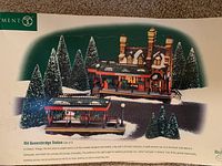Top side view of original box highlighting artwork and descriptive text for Old Queensbridge Station set by Dept 56 with snowy pine trees and detailed building scene.