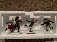 Four porcelain skating figurines in white styrofoam tray inside original packaging box