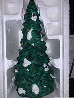 Close-up photo of the green Dept 56 Christmas tree decoration with embedded multi-colored lights and snow accents on branches.