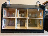 Front view of the dollhouse showing multiple rooms, stairways, and doors with windows on both floors.