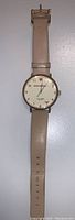 Full view of the Kate Spade wristwatch showing taupe leather strap and round watch face with gold-tone bezel.