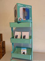 Photo showing the sea foam colored utility cart with boxed two portable heaters, one boxed light, and the boxed mini fridge on top.