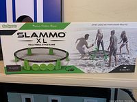 Photo showing the front of the Slammo XL game box with branding, product image, and people playing on sand.