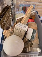 Top view of a bin with various wooden cutouts, styrofoam ball, boxed miniature lights, and gift wrap supplies.