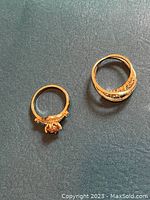 Two sterling silver cocktail rings with rose tint finish placed on a dark surface showing rose-shaped and twisted designs.