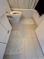 Photo of two bathroom mats placed on a tiled bathroom floor, one larger mat near the sink and toilet, and a smaller mat near the bathtub/shower.