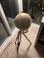 Photo of a hand-made 2-foot diameter globe on a metallic tripod stand indoors by a window with bookshelves nearby.