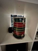 Photo of two handmade tabla hand drums with colorful stripes on wooden shells and metal tuning hardware placed on white shelf