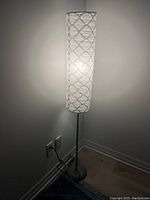 Tall floor lamp in corner with lit fabric shade showing geometric diamond pattern