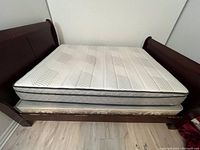 View of queen size therapy mattress with box spring on wooden bed frame, showing mattress surface and box spring upholstery.