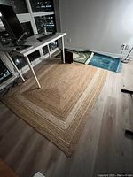 Rectangular cream-colored woven rug displayed under a desk with city view windows in background, showing texture and pattern.