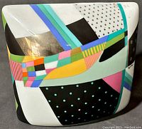 Front view of the square porcelain pillow vase showing vibrant postmodern geometric pattern in multiple colors with gold accents.