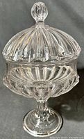 Front angled view of the antique pressed glass covered compote, showing pedestal base and detailed vertical rib pattern on glass.