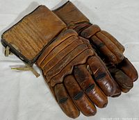 Pair of vintage brown cowhide leather hockey gloves, top view showing padded fingers and cuffs.