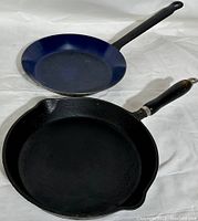 Two frying pans placed on a white background, showing top surfaces and handles.