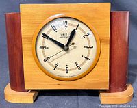 Full front view of the two-tone wooden mantel clock showing the wooden case and clock face with United Self Starting branding.