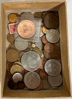 Box containing mixed coins including large silver-colored coins, a Michigan commemorative cent in plastic holder, and smaller brass and copper coins.