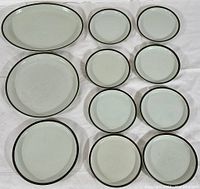 Top view of eleven Denby stoneware plates arranged on a white background showing different sizes from 6.5 to 13 inches with dark rim detail.
