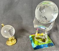 Two etched glass globes displayed on their respective stands against dark background.