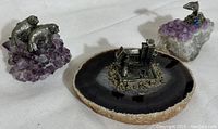 Three natural mineral pieces including two amethyst clusters with pewter sea lion figurines and one polished agate slice with a pewter industrial scene figurine.