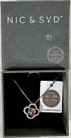 Nic & Syd branded gray box with necklace inside, showing the daisy-shaped pendant with a light topaz Swarovski crystal center and authenticity tag.