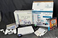Original box of Sony PlayStation 2 Ceramic White with wireless controller, console, power adapter, memory card, game disc, and cables.