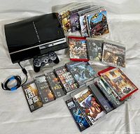 Full view of Sony PS3 console, controller, cables, and 18 PS3 games arranged on white surface.