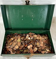 Open green steel cashbox filled with a pile of old pennies inside.