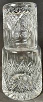 Clear cut crystal bedside carafe with intricate etched designs and matching tumbler positioned on top.