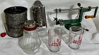 Shows full assortment of vintage kitchen tools including a metal sifter, graters, apple peeler, measuring cups and shaker.