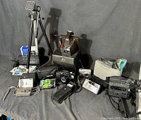 Lot of vintage cameras, accessories and tripod arranged on dark cloth.