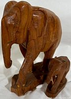 Front and side views of the large and small teak carved elephant statues on a single base.