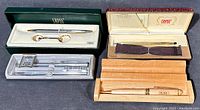 Full lot view showing all three pen sets: Cross with keychain in green case, Sheaffer set in clear plastic case, and Pairo pen in wooden box with paperwork.
