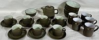 Full set arrangement showing cups, saucers, mugs, bowls, and teapot with chevron pattern in matte olive green stoneware.