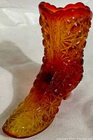 Front angled view of the Fenton glass boot showing the Amberina gradient and Daisy Button textured pattern.