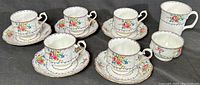 Set of five Royal Albert Petit Point cups paired with matching saucers, arranged on a dark surface with accompanying open sugar bowl and mug in the background.