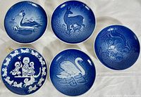 Five circular blue and white porcelain Mother's Day plates laid out on white fabric, each with unique animal or mother-child themed design.