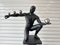 Front view of kneeling figure showing three small spheres on right forearm and one large sphere in left hand.