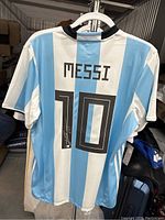 Full rear view of blue and white striped Argentina jersey hanging on hanger in storage setting