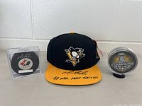 Overview of three items: signed Team Canada puck in case at left, Penguins cap center, Stanley Cup Champions puck in case at right