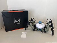 Photo of MekaMon robot with original box behind it, showing full robot and box in neutral background.