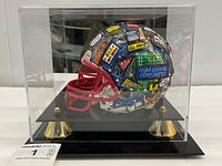 Front view of mini helmet inside acrylic case showing painted graphics and base