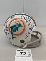 Side view of white Miami Dolphins mini helmet with teal and orange stripes, Dolphins logo, multiple blue ink signatures