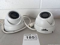 Two white dome security cameras with cables shown from front and side angles. Visible IR LED ring and lens with Watchnet Mpix branding.
