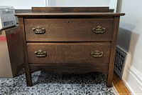 Front view of small wooden dresser with two drawers and metal handles.