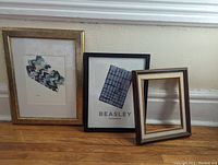 Two framed Hamilton-themed art pieces and one extra empty frame arranged on a ledge