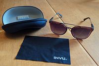 Photo showing sunglasses laid out with case and cleaning cloth on a wooden surface.